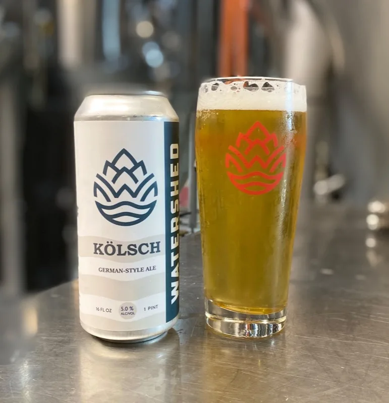 Kölsch German-Style Ale can and glass in front of brewery tanks